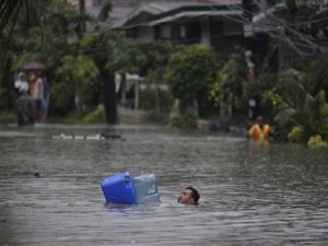 A man crosses deep floodwaters using water containers as floaters in suburban Quezon City, north of Manila, Philippines on Tuesday Aug. 7, 2012. Torrential rains pounding the Philippine capital on Tuesday paralyzed traffic as waist-deep floods triggered evacuations of tens of thousands of residents and the government suspended work in offices and schools.(AP Photo/Aaron Favila)