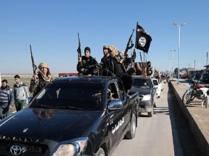 In this photo released on May 4, 2015, by a militant website, which has been verified and is consistent with other AP reporting, Islamic State militants pass by a convoy in Tel Abyad town, northeast Syria. In contrast to the failures of the Iraqi army, in Syria Kurdish fighters are on the march against the Islamic State group, capturing towns and villages in an oil-rich swath of the country's northeast in recent days, under the cover of U.S.-led airstrikes. (Militant website via AP)