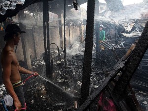 BASAK PARDO FIRE/AUG. 12, 2016: Bryle Bustamante (left) uses his hose in helping fire fighter in doing finishing touches in the burned house owned by Fe Erida at sitio bamboo village barangay Basak Pardo as they do finishing touches.(CDN PHOTO/JUNJIE MENDOZA)